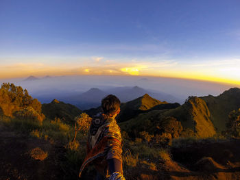 Rear view of man standing on mountain against sky during sunset