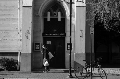 Side view of man walking against building on sunny day