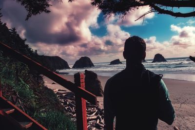 Rear view of man standing by sea against sky