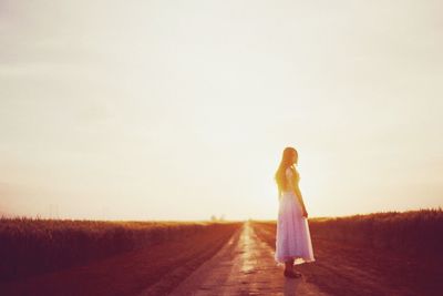 Full length of woman standing on field at sunset