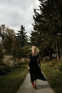 Rear view of woman walking in park against sky