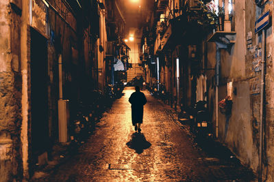 Rear view of man walking on narrow street amidst buildings
