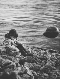 Boy holding balloon while sitting on shore at beach
