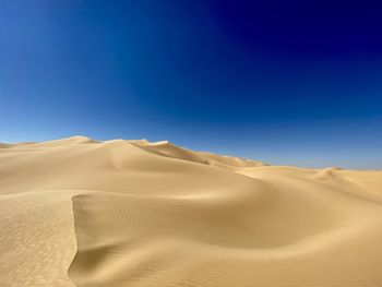 Sand dunes in desert against clear blue sky