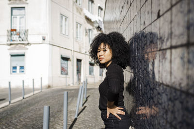 Young woman with hand on hip standing in front of wall