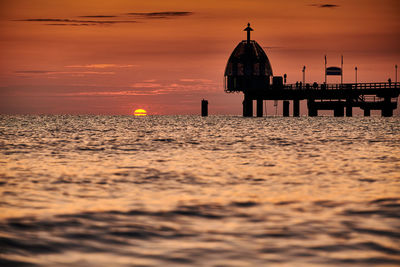 Silhouette building by sea against sky during sunset