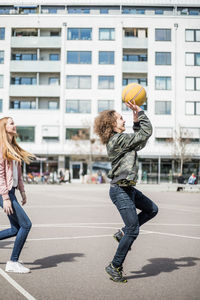 Full length side view of friends playing basketball against building