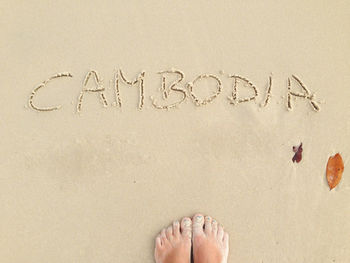 Low section of woman standing by cambodia text at beach