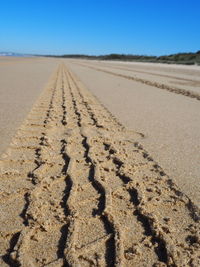 Footprints on sand at beach against clear sky