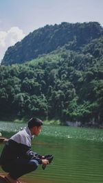 Man sitting by lake against mountains