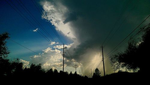 Low angle view of electricity pylon against cloudy sky