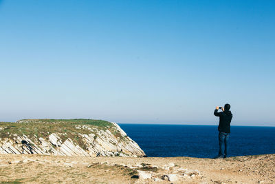 Rear view of man photographing at beach against clear blue sky