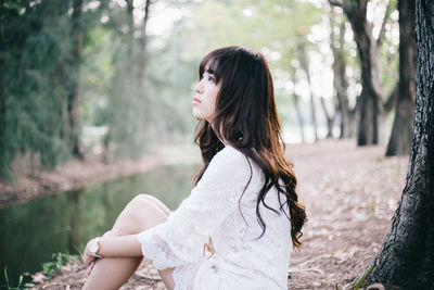 Side view of thoughtful young woman sitting at stream in forest