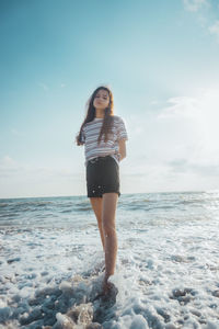 Portrait of young woman standing in sea against sky during sunny day