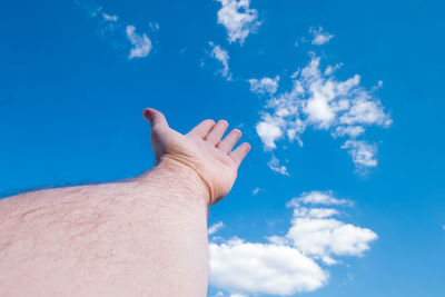 Cropped hand of man gesturing against blue sky