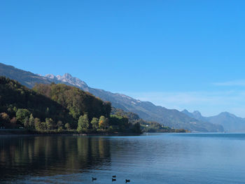 Scenic view of lake and mountains against clear blue sky