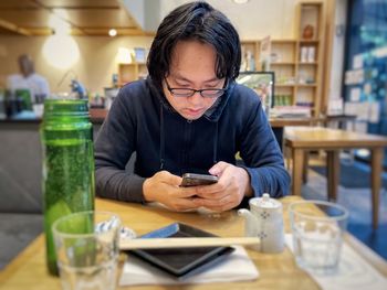 Young asian man using mobile phone at table in cafe.