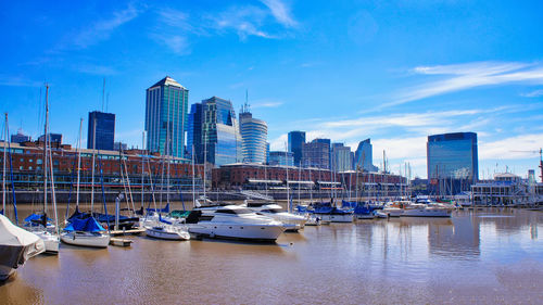 Boats moored in city by buildings against sky