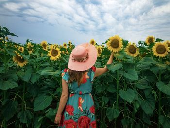 Rear view of woman wearing dress and sun hat in a field of sunflowers on a cloudy day