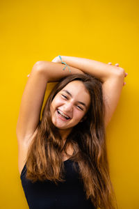 Young woman with arms raised standing against yellow background