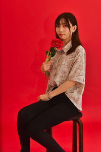 Young woman sitting against red wall