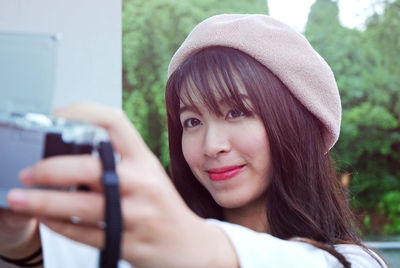 Beautiful woman photographing through digital camera outdoors