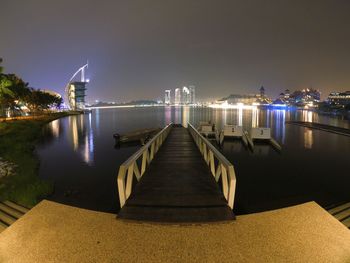 Illuminated city by sea against clear sky at night