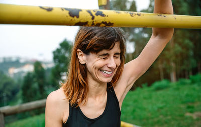 Woman with eyes closed laughing by rod against trees