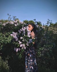 Beautiful woman standing by flowering plants against sky