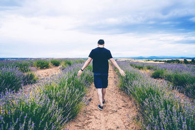 Rear view of man standing on field against sky