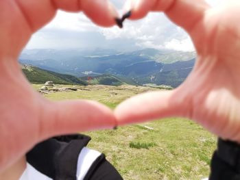 Cropped image of hand on landscape against mountain range