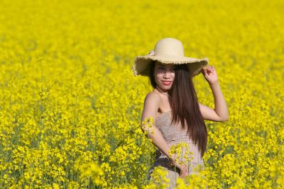 Portrait of young woman touching yellow flowers in field