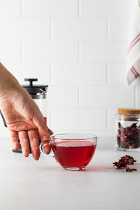 A woman's hand takes a cup with red herbal tea made of hibiscus petals.