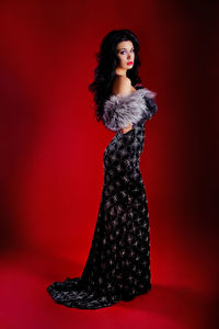 Side view of woman in black dress standing against red background