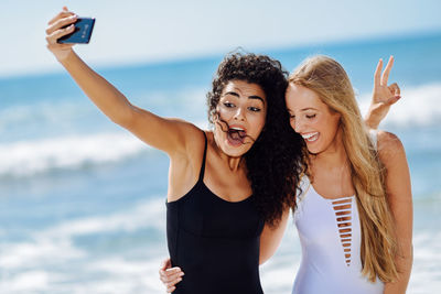 Happy young woman with friend taking selfie standing at beach