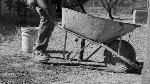 Low section of man with wheelbarrow walking on field