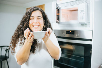 Portrait of smiling young woman holding food in front of oven