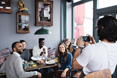 Owner photographing smiling friends through mobile phone at table in restaurant