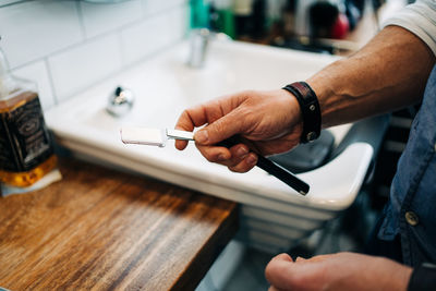 Crop unrecognizable male stylist holding straight razor with sharp blade in beauty salon in daytime