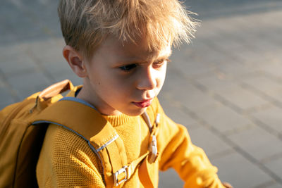 Portrait of an upset little boy in a yellow sweater at sunset.