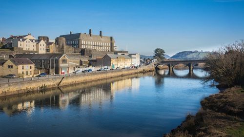 Bridge over river by buildings against clear sky