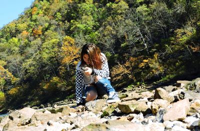 Woman sitting on rock against trees