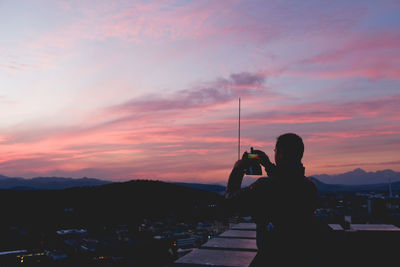 Silhouette of man sitting on mountain at sunset