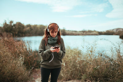 Young woman listening to music with headphones near a lake with her smartphone