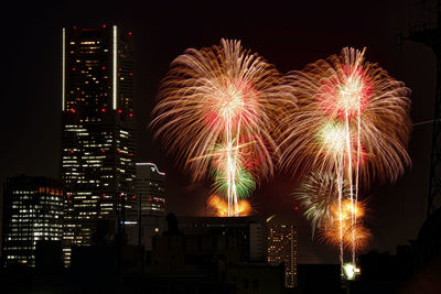 Firework display in city against sky at night