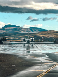 A small jet plane is sitting on the runway in front of a mountain range. 