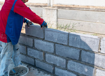 Bricklayer worker installing brick masonry on exterior wall in building site.