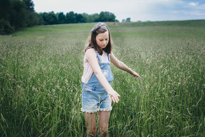 Girl running her hands through tall grass in a field in the midwest