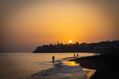Silhouette people on beach against sky during sunset