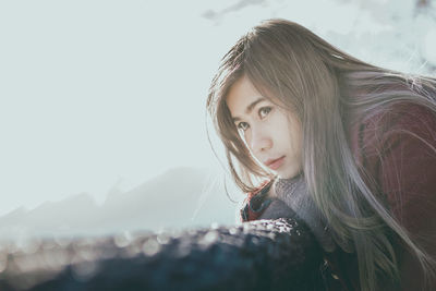 Thoughtful mid adult woman leaning on retaining wall against sky during sunny day